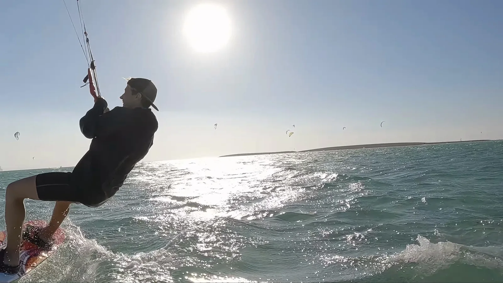 Kiter v protisvětle těsně u kamery, za ním slunce a další kity
